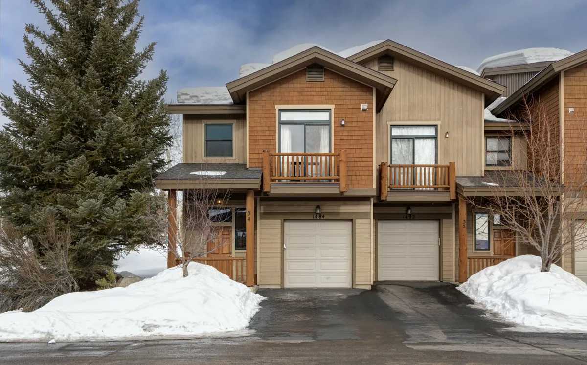 This exterior winter scene shows the wooden balconies of Cornerstone 34 overlooking a snow-covered yard framed by a tall evergreen tree. The balconies suggest private spaces for adults to relax, while the open yard hints at room for children to play and families to gather for outdoor activities.