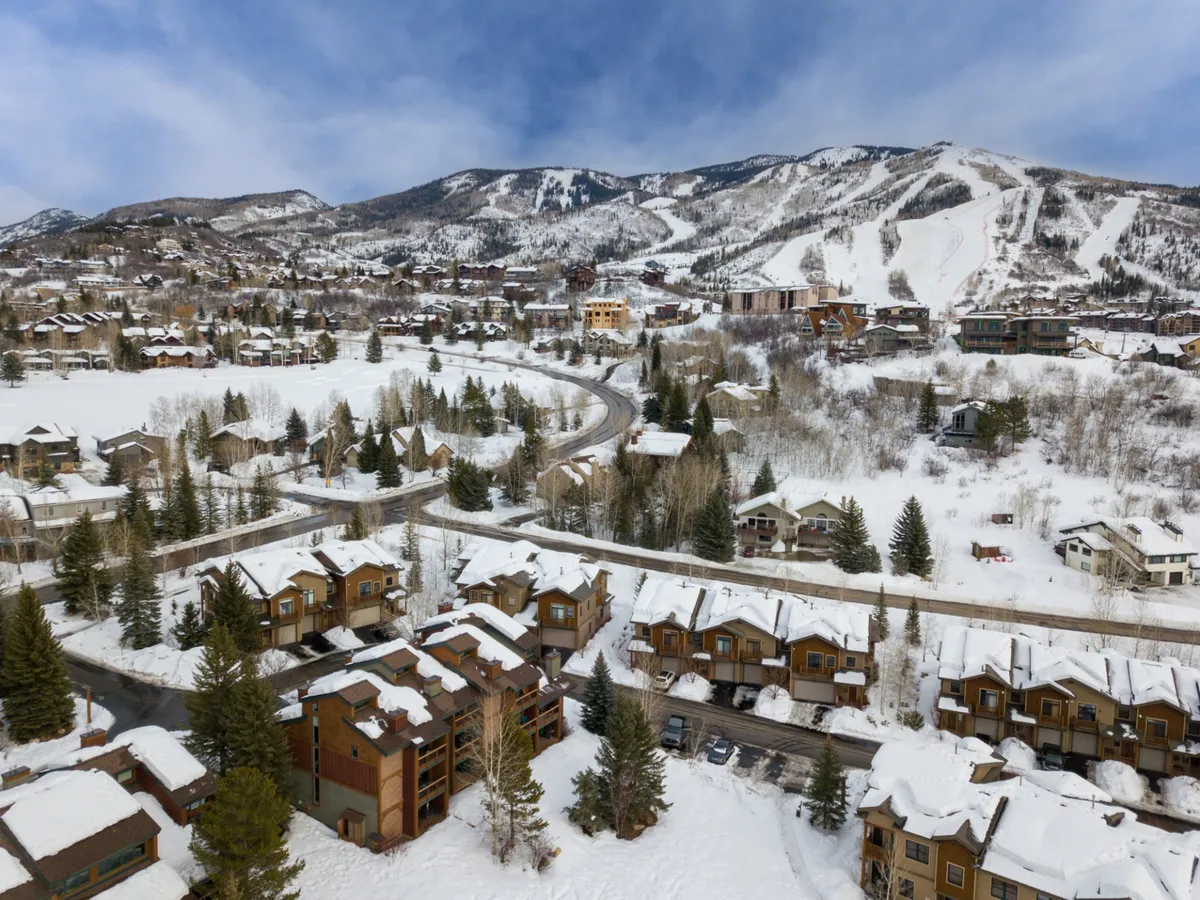 A scenic view of snow-covered mountains, tree-lined streets, and charming wooden houses paints a classic Steamboat Springs winter scene. The snowy landscape is inviting for skiing, snowboarding, and exploring nature trails.