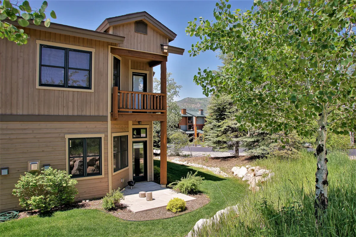 An exterior shot showing a wooden balcony, large windows, and lush greenery, suggesting seamless indoor-outdoor flow. The area is ideal for barbecues and gatherings, and the visual connection to the interior supports year-round enjoyment as described in the section.