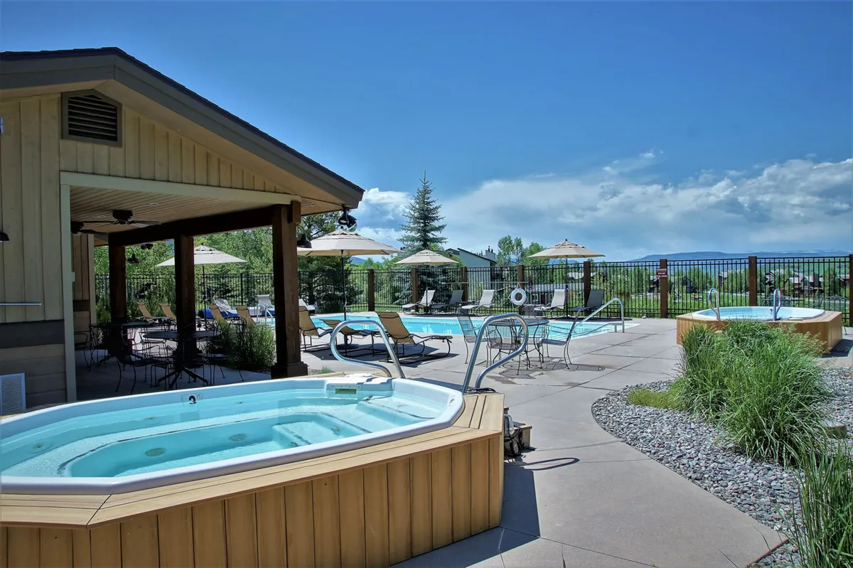 This exterior shot highlights both the hot tubs and swimming pool, with lounge chairs and umbrellas arranged nearby. The scene feels tranquil and inviting, emphasizing spaces ideal for soaking year-round or lounging with friends after outdoor adventures.