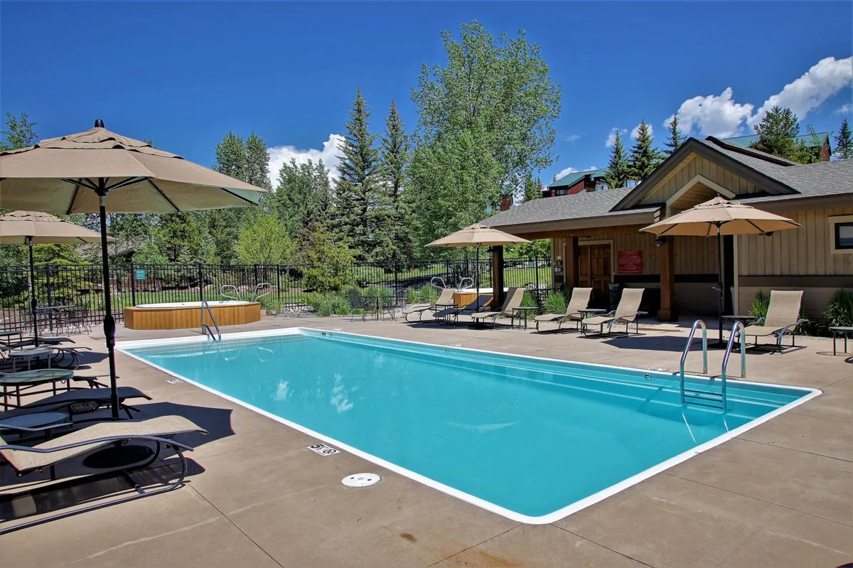 This image showcases a vibrant community swimming pool surrounded by sun loungers, umbrellas, and lush landscaping. The pool area has an inviting and sociable atmosphere, with spaces for both swimming and sunbathing, perfect for summer relaxation or gathering with neighbors.