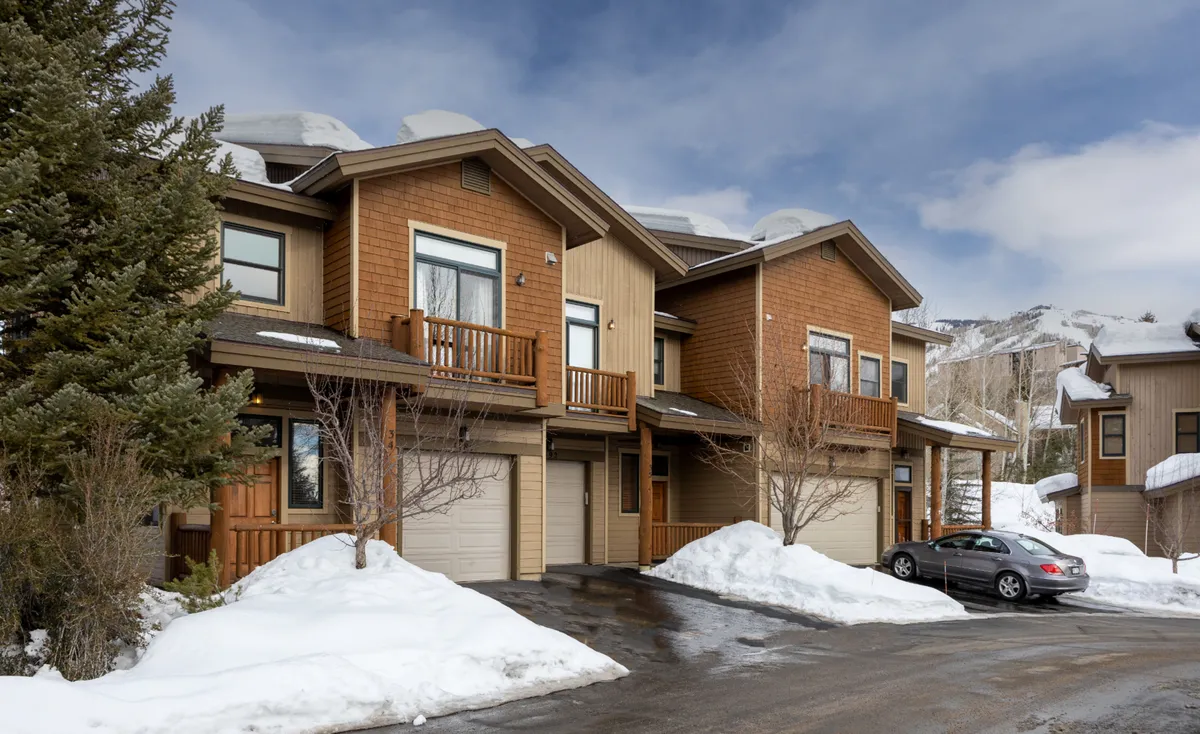 A cozy exterior shot featuring modern wooden balconies overlooking a snow-covered ground, with a warm golden glow from inside. The scene suggests residents returning after a day on the slopes, ready for après-ski relaxation.