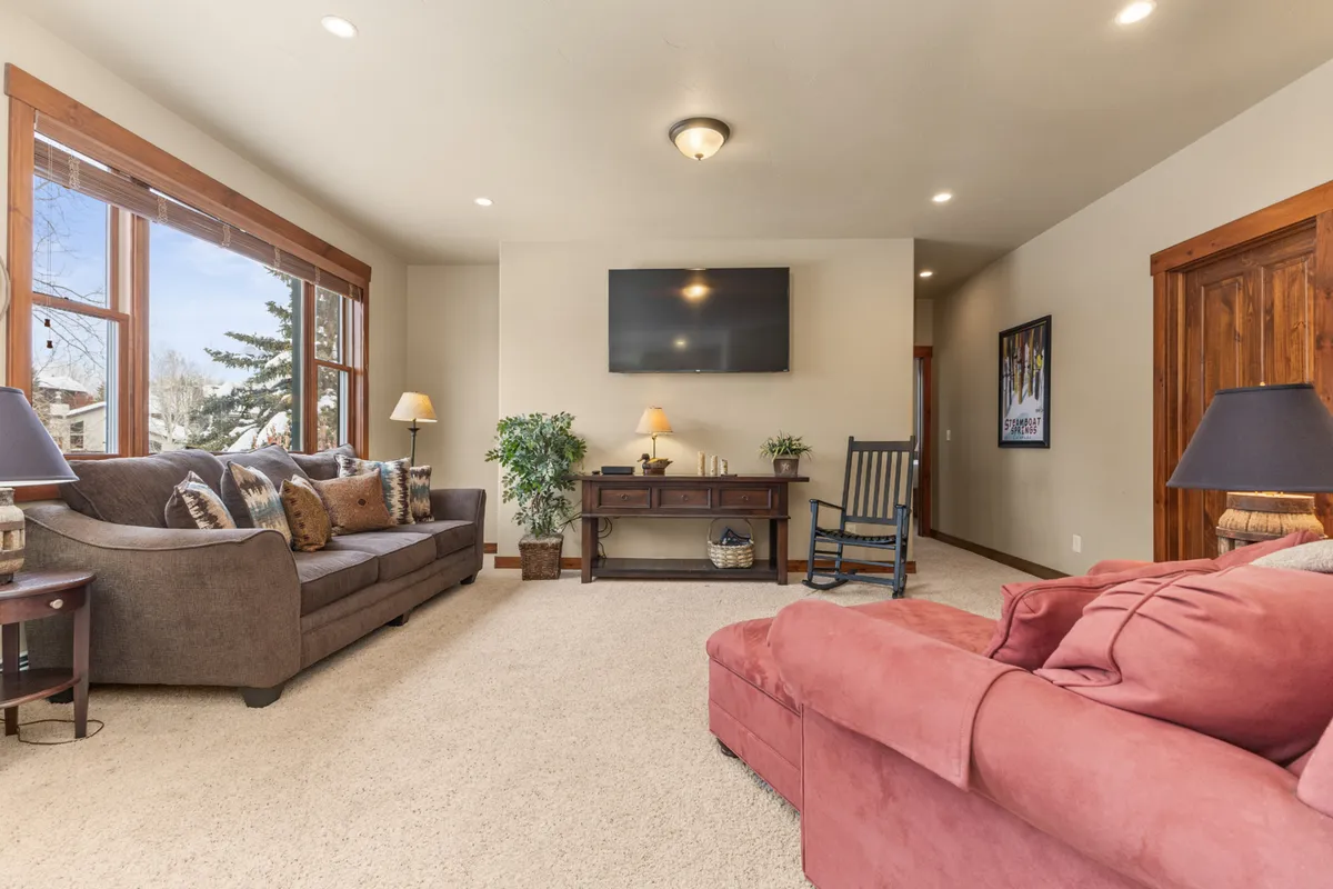An upstairs living room with a plush sofa, coffee table, television, and a window adorned by a flourishing houseplant. The space feels cozy and intimate, tailored for relaxation, media enjoyment, or quiet retreat.