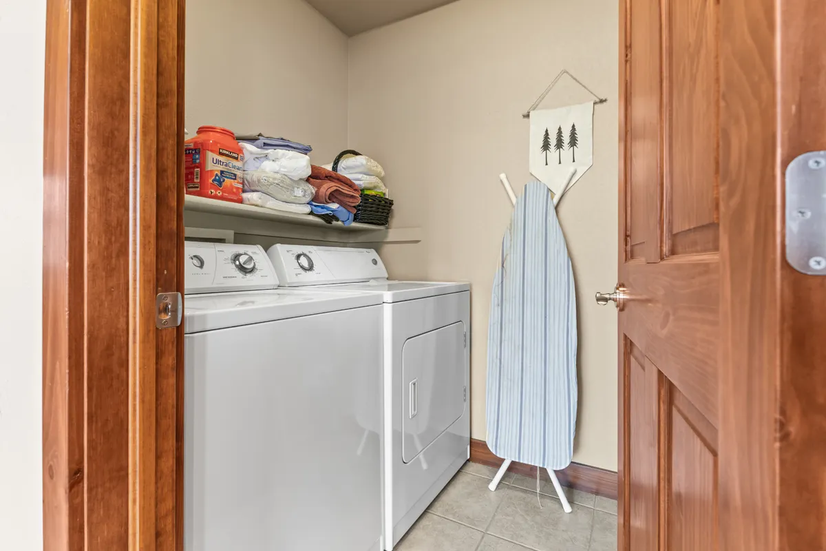 A practical, tidy laundry room with a washing machine, dryer, ironing board, and shelves stocked with fresh towels. The space is organized and welcoming, underscoring the home's convenience for longer stays.
