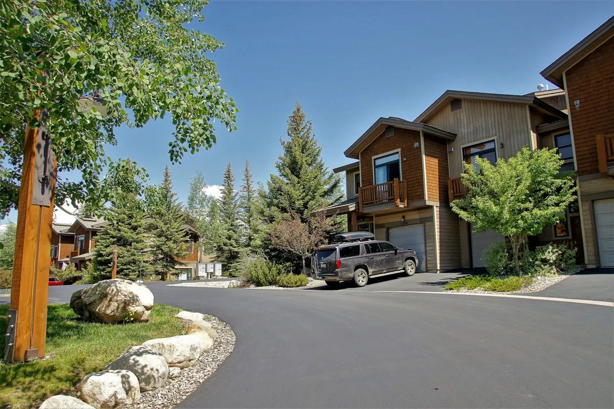 The image depicts the welcoming exterior of the townhouse, landscaped garden, driveway, and parked vehicle. The scene hints at outdoor relaxation, barbecuing, and social gatherings, set against the backdrop of nature and comfort.