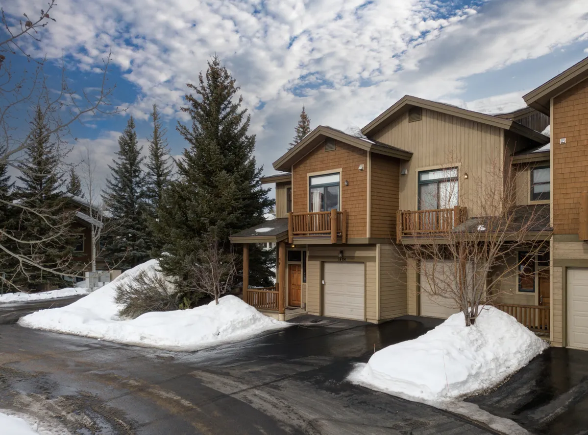 A cozy wooden exterior of the townhome nestled among tall evergreen trees with snow covering the ground. The balcony looks inviting for stargazing or enjoying the tranquil setting, and the scene conveys a sense of peace and privacy in a mountain environment.