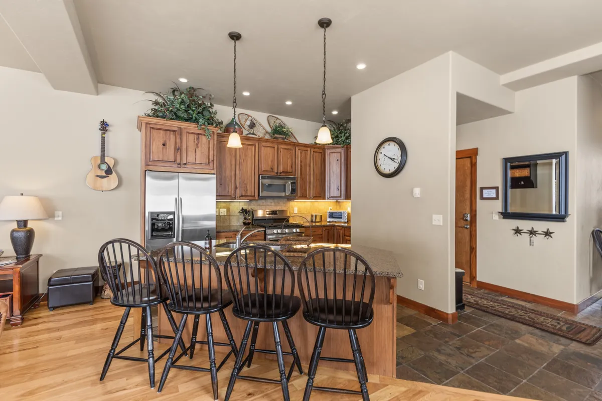 A view of a modern kitchen with a large island and bar stools for casual dining, stainless steel appliances, and inviting decor. The space is designed for both cooking and socializing, echoing the 'well-equipped kitchen' and 'effortless group connection' described.