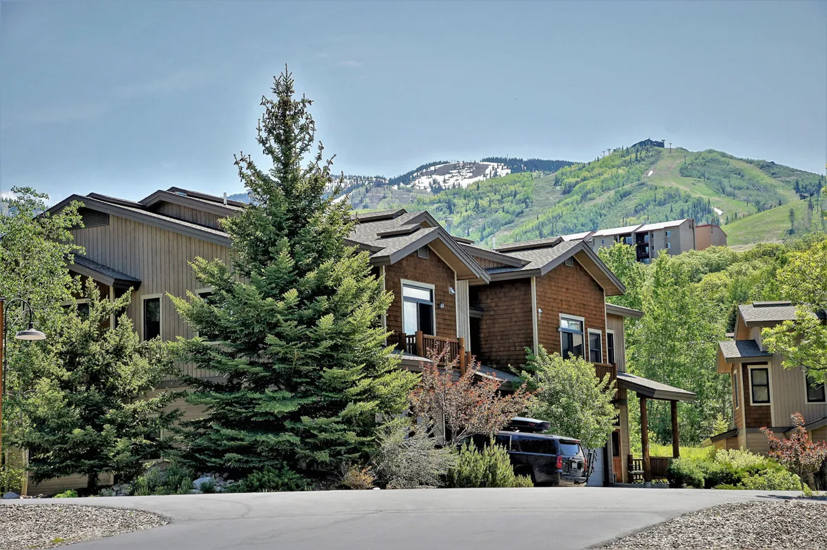 The image showcases the inviting exterior of a spacious end-unit townhome nestled among tall pine trees, with an expansive mountain backdrop. The serene outdoor area hints at space for relaxing on the porch, stargazing, and enjoying barbecues, all enveloped in a tranquil, natural setting.