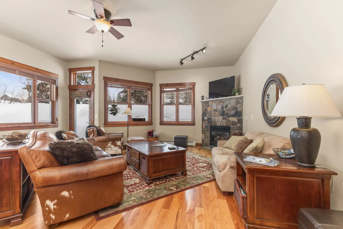 An inviting living room interior with leather sofas, a stone fireplace, a coffee table, and large windows showing snow outside. The spacious arrangement is ideal for group activities like family movie nights, board games, and holiday celebrations.